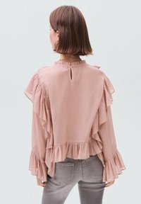 Camicetta rosa con volant in tessuto testurizzato, caratterizzata da uno scollo a chiave sul retro, maniche lunghe e volant a strati lungo le spalle e l'orlo.