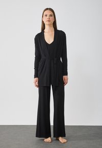 Černý loungewear set obsahující kardigan s dlouhým rukávem a zavazováním v pase, top s hlubokým V-výstřihem a kalhoty s širokými nohavicemi, vše z měkkého, splývavého materiálu.