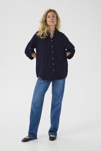 Navyblaues Langarm-Hemd mit Knöpfen und Tasche, kombiniert mit hellblauen, geraden Jeans und schwarzen Ballettschuhen. Sanfter Stoff mit glatter Textur.