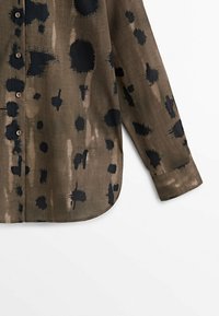 Kuosisormustettu nappipaita teksturoidusta ruskeasta kankaasta, jossa on abstrakteja mustia läiskiä ja siveltimen jälkiä, kaarevalla helmalla ja pitkillä hihoilla.