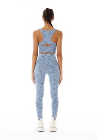 Blå atletisk uppsättning bestående av en sport-bh med racerback och högmidjade leggings med en texturerad, melerad mönstring. Vita sportskor är synliga.