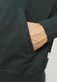 Dark gray sweatshirt with a front pocket, ribbed cuffs, and a tag at the hem. Fabric appears soft, with visible stitching details.