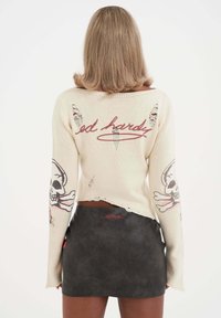 Crème gebreide trui met verstoorde accenten, voorzien van een doodskopfprint op de mouw en het "ed hardy" logo. Gecombineerd met een zwarte nep leren minirok.