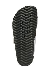 Suela de goma negra con patrón de zigzag, que presenta orificios para la transpirabilidad y un logo de la marca en relieve. Tiras blancas visibles en los lados.