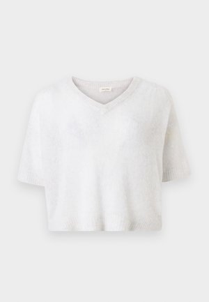 Pull en maille blanche douce à manches courtes avec col en V et coupe légèrement courte sur un fond uni.