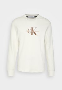 Felpa bianca a maniche lunghe in tessuto a nido d'ape con logo marrone "CK Calvin Klein Jeans" centrato sul petto.
