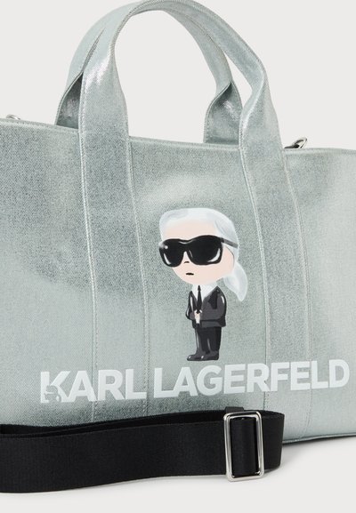Сребристосива чанта тип тоут на Karl Lagerfeld с анимационна фигура, бяло лого, къси дръжки и черна регулируема презрамка за рамо.