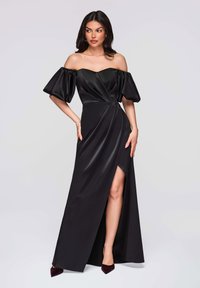 Robe en satin noir avec manches bouffantes épaules dénudées, corsage ajusté et fente haute à la cuisse. Présente un design drapé et une finition élégante.
