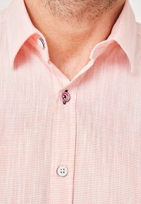 Helles rosa kariertes Hemd mit Button-Down-Kragen. Auffällige Details sind ein kontrastierender Knopf und eine subtile Textur.