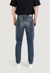 Jeans de mezclilla azul ajustados con bolsillos traseros, costuras visibles y un ligero desgaste, combinados con zapatillas blancas y una camiseta negra.