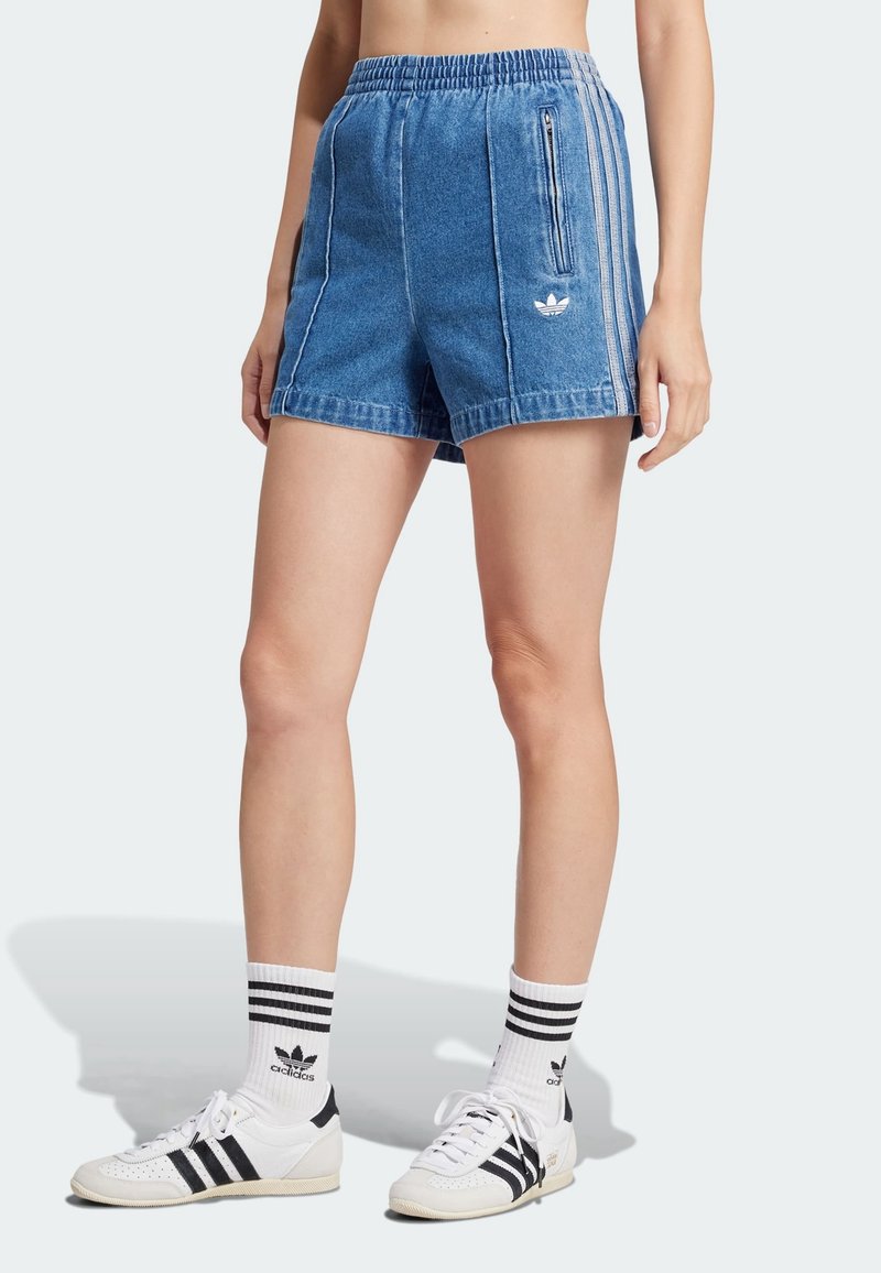 Pantalones cortos de mezclilla de color azul claro con una cintura elástica, bolsillos laterales y rayas blancas. Combinados con zapatos deportivos en blanco y negro y calcetines.
