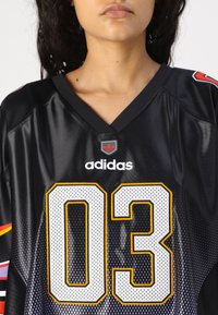 Fekete sportpóló rövid ujjal, V-nyakkal, Adidas logóval, nagy fehér és sárga "03"-as számmal, valamint pöttyös textúrával.