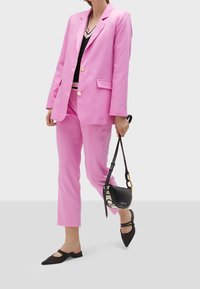 Rosa skräddarsydd kostym med en ensidig kavaj och matchande slim-fit byxor, i kombination med svarta platta skor och en liten axelväska.