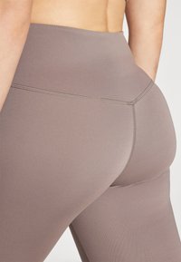 Leggings a vita alta di un colore taupe tenue, realizzati in tessuto elasticizzato. Presentano cuciture piatte e una texture liscia, che esalta la vestibilità.