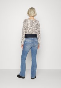 Camisa de manga longa com estampa de leopardo e decote redondo, combinada com jeans flare azuis claros. Cintura preta e botas largas pretas.