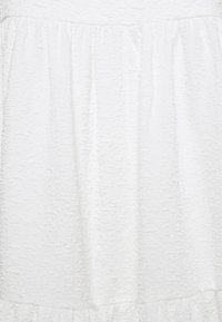 Λευκό φόρεμα με υφασμάτινη υφή, διαθέτει συγκεντρωμένη μέση και ριχτό στρίφωμα. Η επιφάνεια έχει ένα διακριτικό, ανάγλυφο σχέδιο.