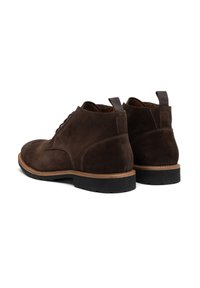 Botas de ante marrón hasta el tobillo con puntera redonda, suela de goma plana, costuras en beige contrastantes y un tirador en la parte trasera para facilitar su calzado.