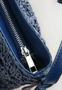 Gros plan d'un sac à main tissé bleu avec une fermeture éclair métallique argentée partiellement ouverte, montrant la doublure intérieure du sac.