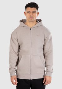 Lichtgrijze rits hoodie gemaakt van zachte stof, met een voorkantzak, rib gebreide manchetten en een aansluitende capuchon. Eenvoudig ontwerp met minimale branding.