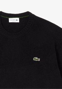 Svart tröja i stickat material med rund halsringning. Har en liten grön och vit Lacoste krokodil-logotyp på bröstet.