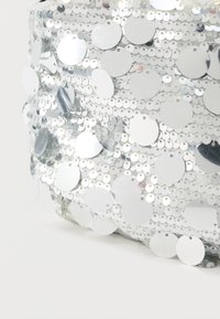 Ύφασμα διακοσμημένο με ασημένιες παγιέτες σε κυκλικό σχήμα, σε διάφορα μεγέθη, που δημιουργούν μια αντανακλαστική και υφασμένη επιφάνεια. Στρογγυλό σχήμα.