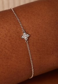 Zilveren armband met een bloemvormige bedel met vijf heldere edelstenen, gelegd op een huidtint van bruin.