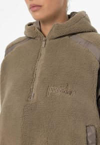 Felpa con cappuccio in fleece beige con design a mezze zip, caratterizzata da una superficie testurizzata e dettagli grigi sulle spalle. Logo ricamato sul davanti.