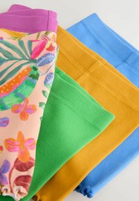 Quatre pantalons en tissu côtelé pliés, de couleurs violet, motif floral, vert, moutarde et bleu, disposés côte à côte sur une surface plane.