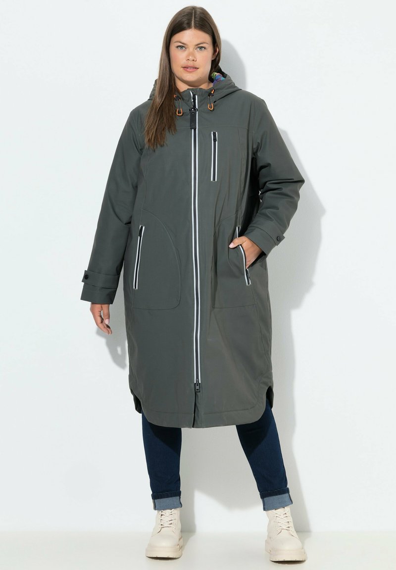 Parka larga de color gris oscuro con cierre de cremallera frontal, dos bolsillos delanteros, capucha ajustable y detalles de ribete blanco en contraste. Tejido suave y resistente al agua.