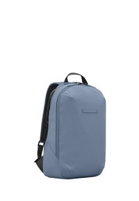 Sac à dos bleu clair avec un extérieur en tissu lisse, forme rectangulaire élégante, poignée supérieure et panneau arrière en mesh pour la ventilation.