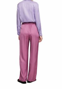 Fialová saténová blůza s dlouhými rukávy a manžetami na knoflíky, spárovaná s vysokým růžovým saténovým kalhotami s volnějším střihem.
