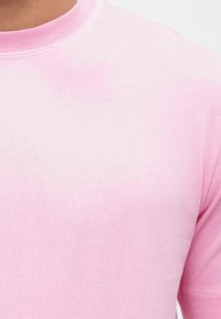 Tricou din bumbac roz deschis, cu decolteu rotund și mâneci scurte; prezintă o textură netedă și un efect subtil de culoare în gradient.