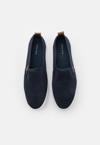 Námořnické slip-on boty s síťovaným svrškem, kontrastními hnědými akcenty a bílou gumovou podešví, navržené pro pohodlí a prodyšnost.