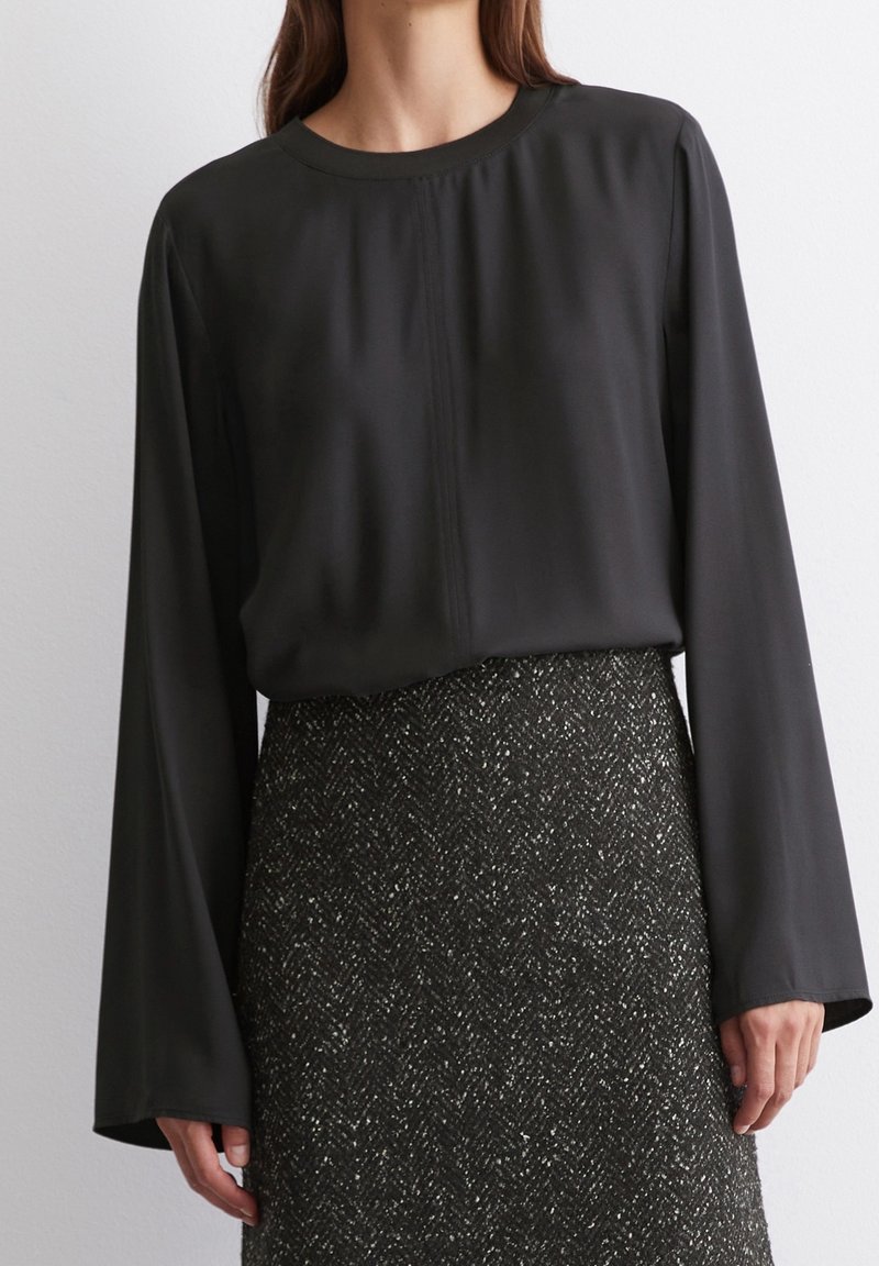 Blusa nera a maniche lunghe con scollatura arrotondata, realizzata in tessuto morbido; abbinata a una gonna scura a fantasia e dalla texture particolare.