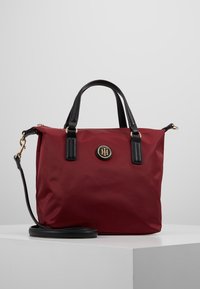 Borsa a mano in nylon rosso con accenti in pelle nera, manici superiori e tracolla removibile. Presenta una placca con logo dorato sulla parte anteriore.