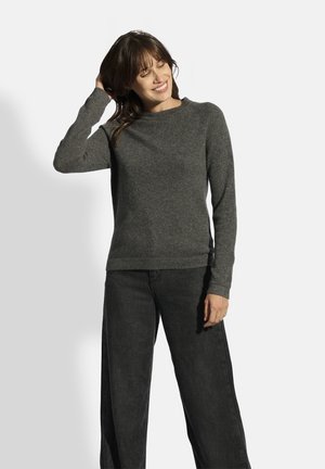Grijze gebreide trui met een ronde hals en lange mouwen, gecombineerd met losse zwarte broek. De textuur lijkt zacht en comfortabel.