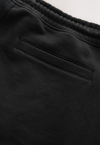 Gros plan sur la ceinture élastique noire et la poche passepoilée arrière sur un pantalon ou un short en tissu doux.