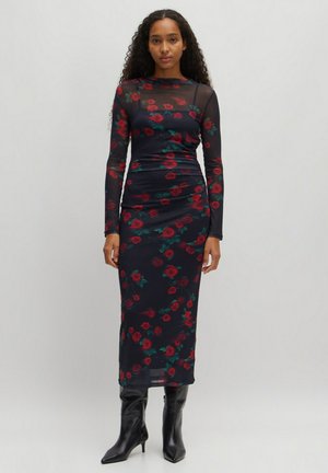 Langärmliges schwarzes Kleid mit rotem Rosenmuster, aus transparentem Material. Figurbetontes Design, knielange Länge, getragen mit schwarzen Stiefeletten mit Absatz.