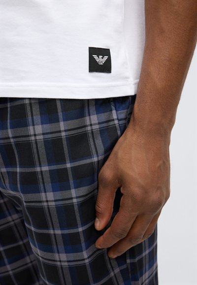 Balta kokvilnas T-krekls ar melnu logotipa tagu, kombinēts ar pleda raksta šortiem zilā, melnā un pelēkā toņos, ar gludu tekstūru.