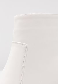 Botín de tobillo blanco de cuero que presenta una textura suave, un diseño minimalista y detalles de costura lateral, con un alto cuello.