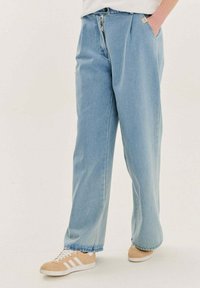 Svetlomodré denimové nohavice s širokými nohavicami, so zipsom a prednými vreckami. Hladká textúra a uvoľnený strih. V kombinácii s béžovými teniskami.