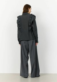 Gray ruffled blouse with a tailored fit, featuring a smooth texture and subtle sheen. Paired with wide-leg gray trousers.