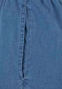 Tela de mezclilla en azul medio, que presenta una costura lateral con detalles de costura doble y una ligera textura en la superficie.