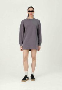 Περίσσειρα γκρίζα φόρεμα φούτερ με μακριά μανίκια, στρογγυλή λαιμόκοψη και πλευρικές σχισμές. Συνδυάζεται με μαύρα αθλητικά παπούτσια και λευκές κάλτσες μέχρι τον αστράγαλο.