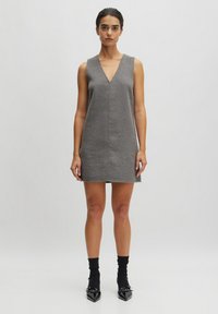 Grijze mouwloze jurk met een V-hals, rechte snit en minimale naden. Gecombineerd met zwarte enkelsokken en puntige schoenen. Gladde textuur.