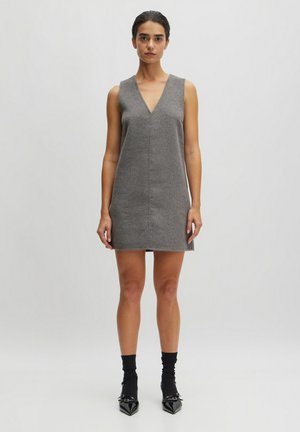 Grijze mouwloze jurk met een V-hals, rechte snit en minimale naden. Gecombineerd met zwarte enkelsokken en puntige schoenen. Gladde textuur.