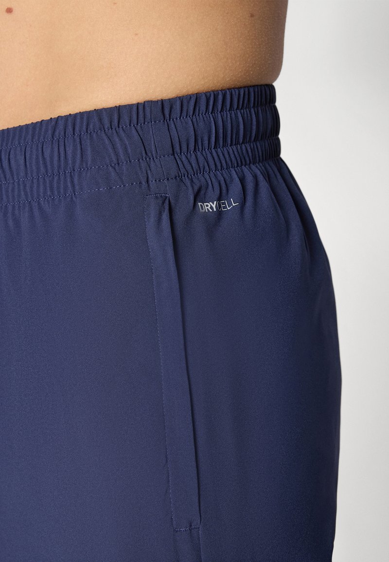 Pantalones cortos deportivos en color navy con cinturilla elástica y bolsillo lateral. Fabricados con un tejido ligero y que absorbe la humedad, con la marca “DRYCELL”. 