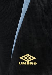 Μαύρο υφασμάτινο υλικό με υφή, με ανοιχτό μπλε διαγώνια ρίγα και το κίτρινο λογότυπο Umbro τυπωμένο κοντά στο κάτω μέρος.