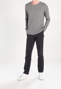 Gray long-sleeve t-shirt paired with dark slim-fit pants and white sneakers, featuring a round neckline and smooth fabric texture.