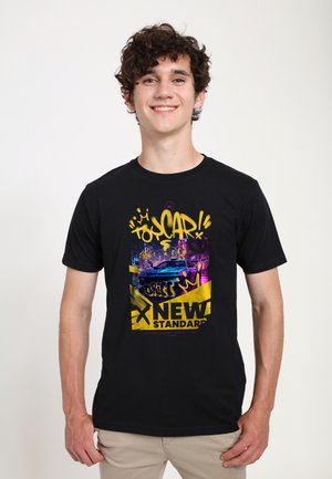 Jeune homme souriant portant un t-shirt noir avec un texte coloré style graffiti et un dessin de voiture de course à l'avant.